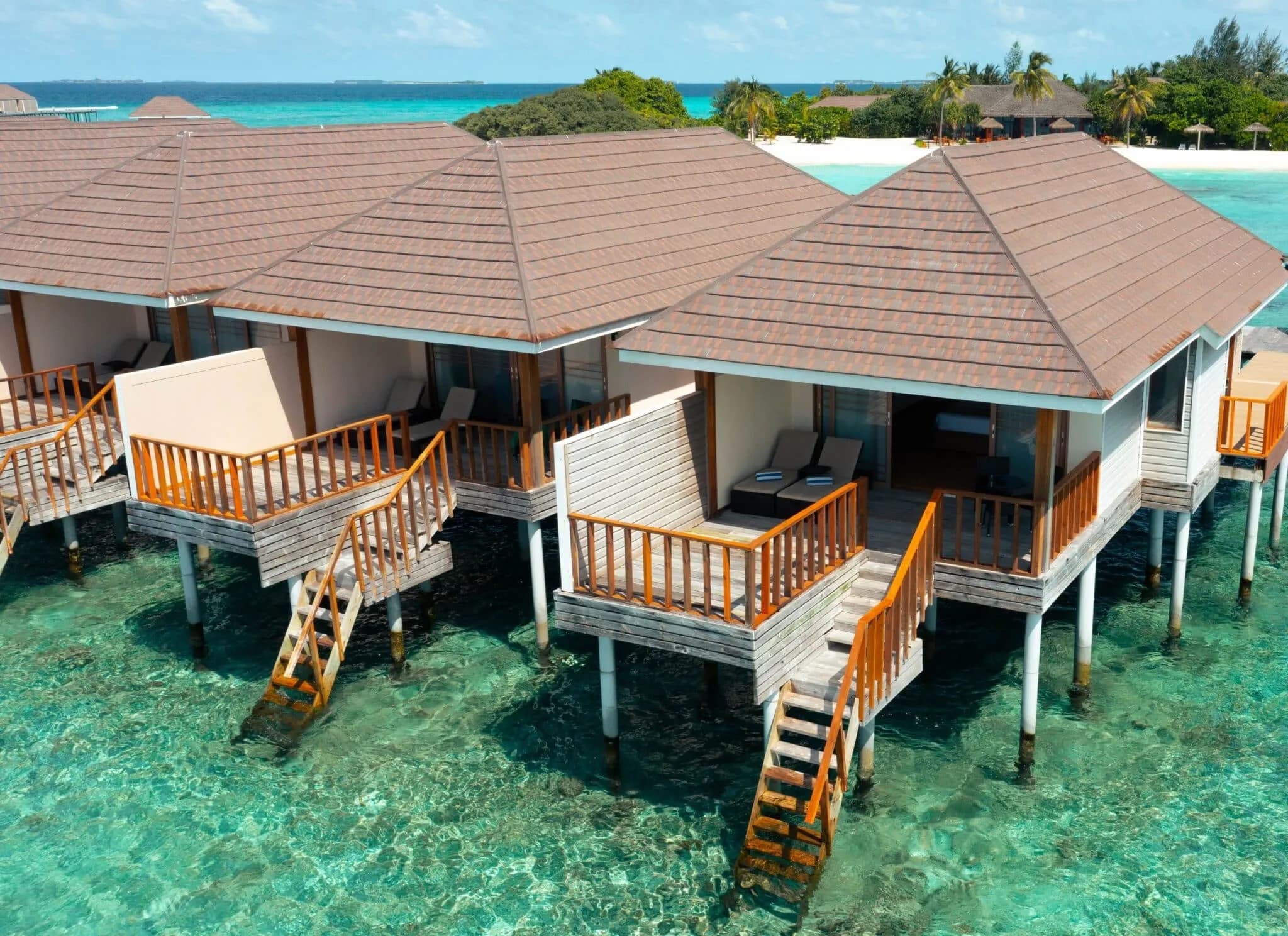Overwater pool villas on stilts above a turquoise lagoon at Brennia Kottefaru