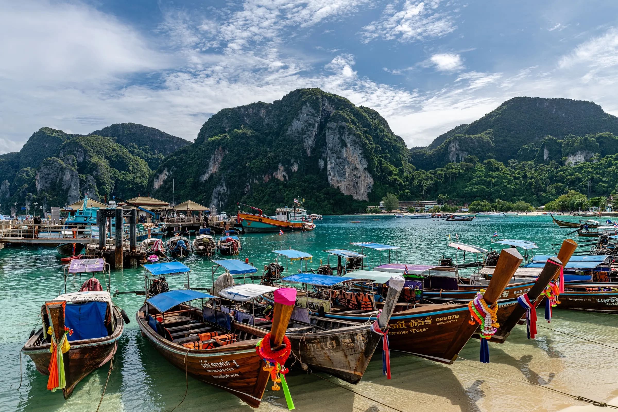 Long-tail boats moored in a turquoise bay below limestone cliffs