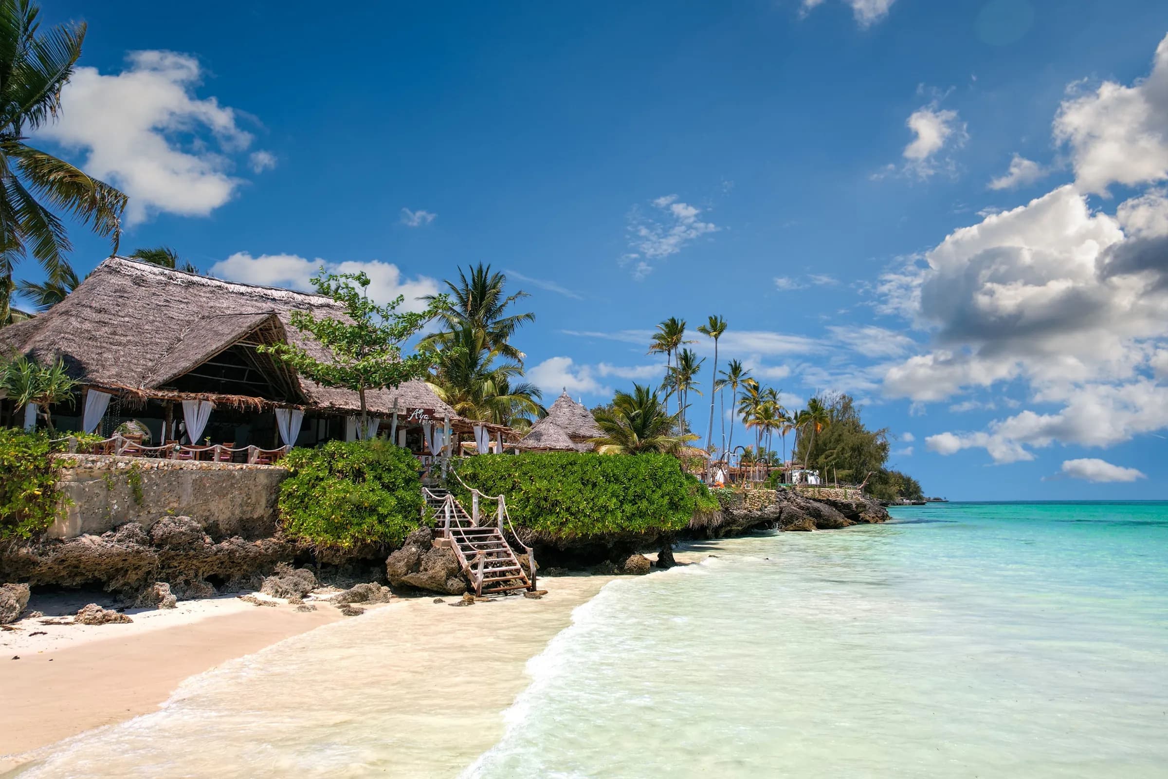 Thatched beach huts and palms above a white sand beach in Zanzibar